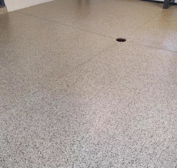 The image shows a terrazzo floor with speckled patterns. A solitary dark brown object, resembling a hair tie, is present near the center.