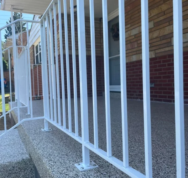 A residential entryway with white metal bars, a pebble-dash porch, a brick wall, and a visible door. The bars seem to function as a safety gate.