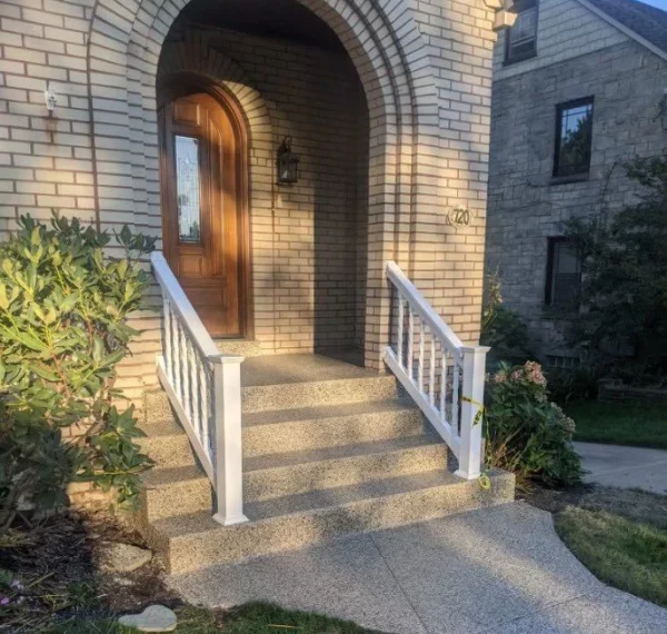 An arched entryway leads to a wooden door numbered 720, with a white railing, steps, and well-maintained shrubbery on a sunny day.