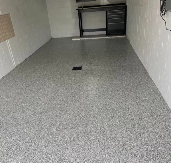 This image shows a clean, empty garage with a speckled epoxy floor coating, white painted walls, and mounted black storage cabinets.