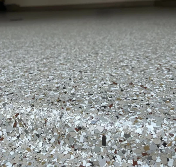This image shows a close-up view of a speckled epoxy floor with a blurred outlet and cable in the background against a white wall.