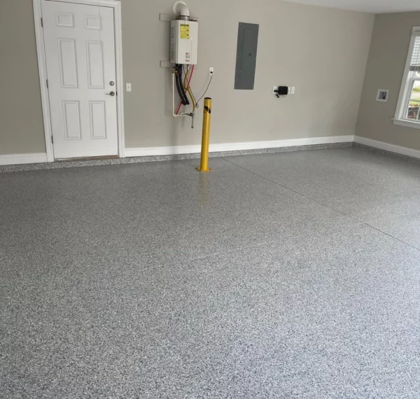 An empty room with a speckled gray epoxy floor coating, white walls, a window, a white door, and visible electrical panels and a water heater.