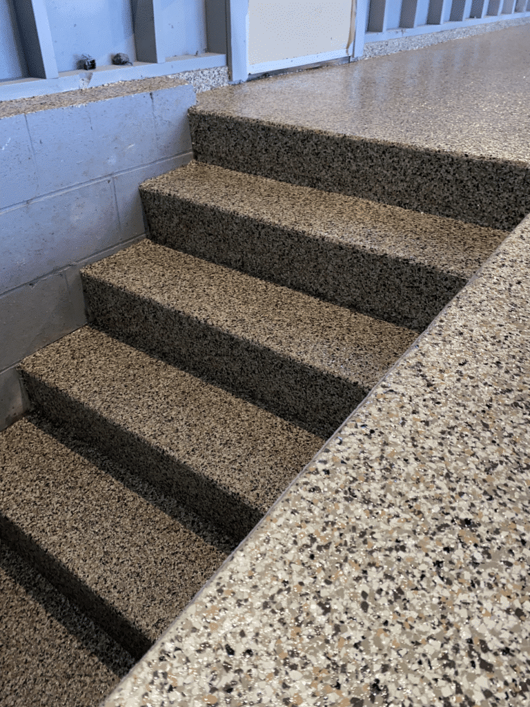 The image shows a set of terrazzo stairs with speckled patterns, leading up to a landing with metal railings, within an interior space.