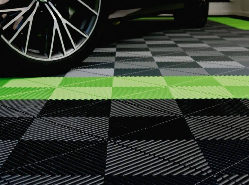 The image shows a patterned floor with interlocking tiles in black, white, grey, and neon green. Part of a vehicle's tire is visible.