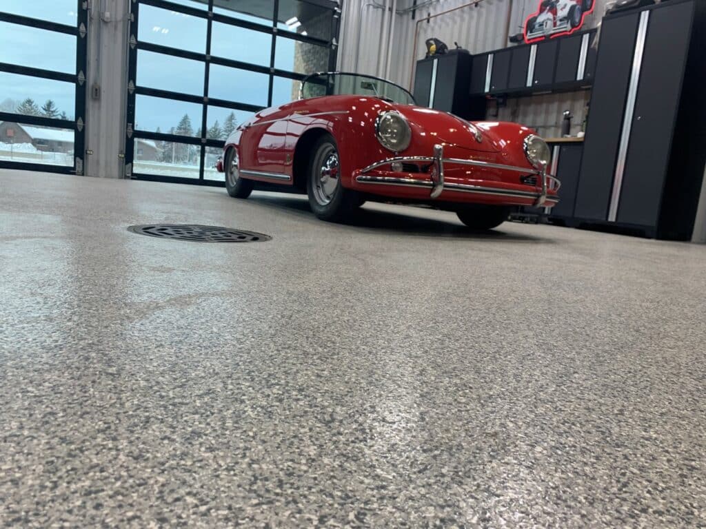 A red vintage convertible car parked on a polished concrete floor inside a building with large windows and a garage-style door partially visible.