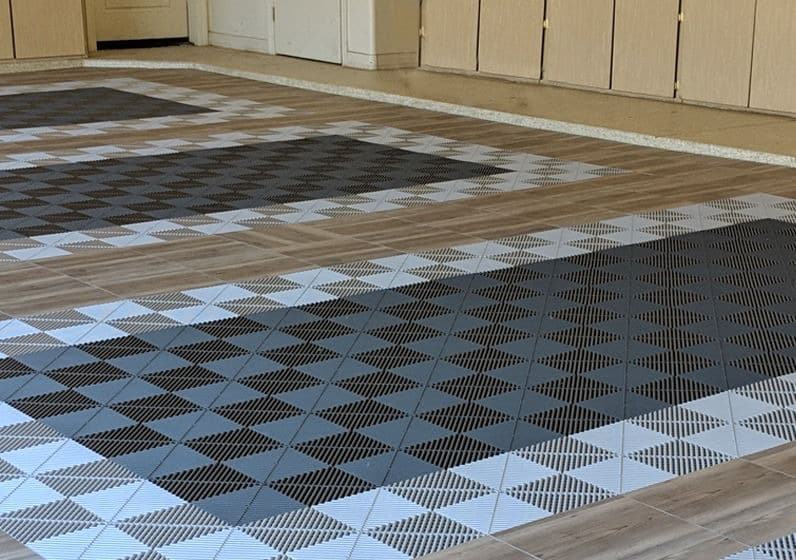 The image shows a floor with a geometric pattern comprised of dark and light square tiles, creating a 3D optical illusion effect near a building entrance.