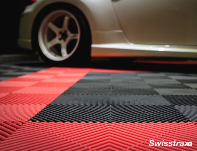 This image features a close-up of a patterned, interlocking floor with a red, black, and grey design, partially underneath a vehicle with visible wheel.