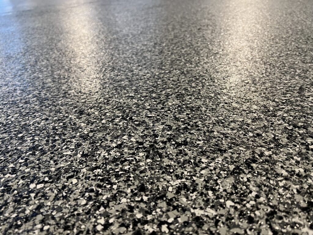 The image shows a close-up of a speckled granite floor with a shiny surface, reflecting light, possibly in a modern interior setting.