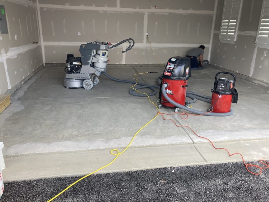 The image shows a garage with drywall and a concrete floor. There are three power tools, possibly vacuums or air compressors, with hoses and electrical cords.