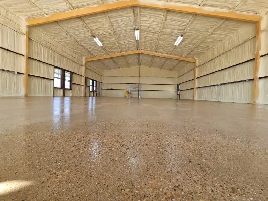 This image shows a spacious, empty indoor hall with a polished concrete floor, timber framing, beige walls, large windows, and a yellow ladder in the distance.