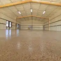 This image shows a spacious, empty indoor hall with a polished concrete floor, timber framing, beige walls, large windows, and a yellow ladder in the distance.