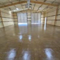 This image shows an empty indoor space with wood-paneled walls, a shiny concrete floor, and large light transmitting panels on a garage door.