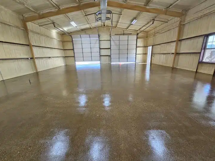 This image shows an empty indoor space with wood-paneled walls, a shiny concrete floor, and large light transmitting panels on a garage door.