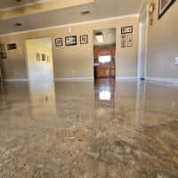 The photo shows an interior space with polished stone flooring, leading to a kitchen area. Walls are adorned with framed pictures. A doorway is visible. No people are in the shot.