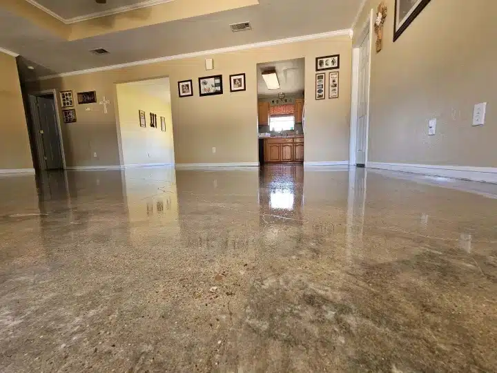 The photo shows an interior space with polished stone flooring, leading to a kitchen area. Walls are adorned with framed pictures. A doorway is visible. No people are in the shot.
