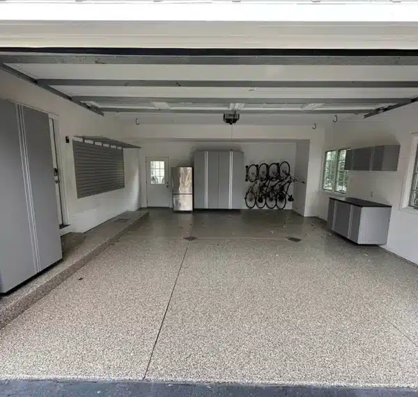 Empty two-car garage with a speckled floor, grey storage cabinets, a few bicycles hanging on the wall, and a closed garage door with windows.