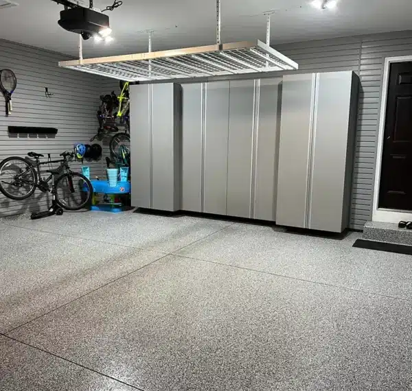 This image shows a tidy garage interior with organized storage cabinets, bicycles, sports equipment, and speckled flooring, with a dark entry door on the right.
