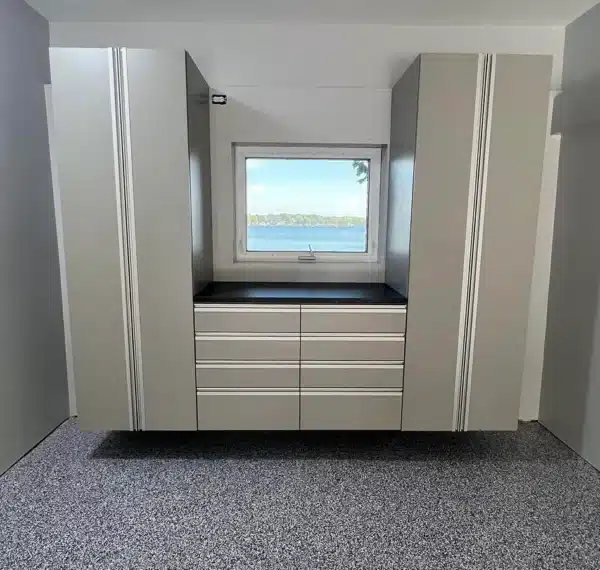 A modern room with a window revealing a water view, flanked by grey built-in cabinets and drawers, over a speckled grey floor.