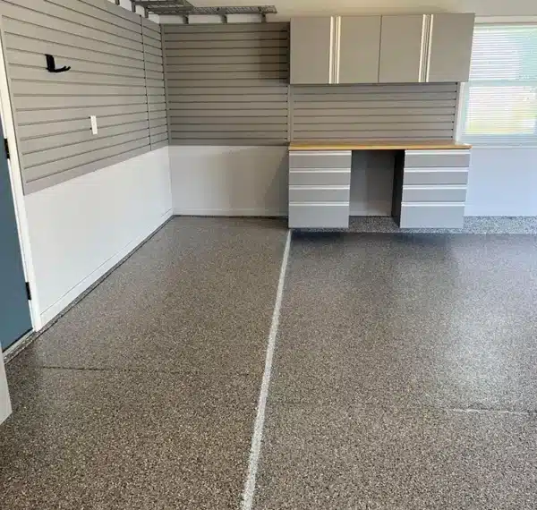 This image shows a tidy, organized garage interior with a speckled epoxy floor, gray storage cabinets, slatwall panels, and a workspace with a countertop.