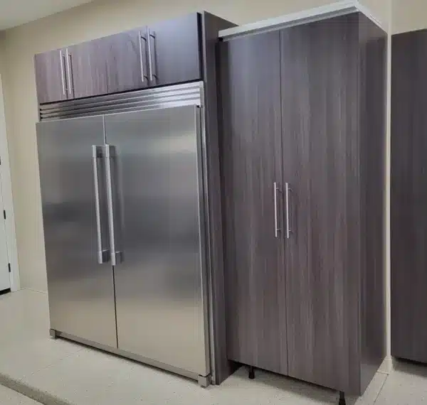A modern kitchen with a stainless steel double-door refrigerator next to a tall, dark-wood cabinet, with white walls and light terrazzo flooring.