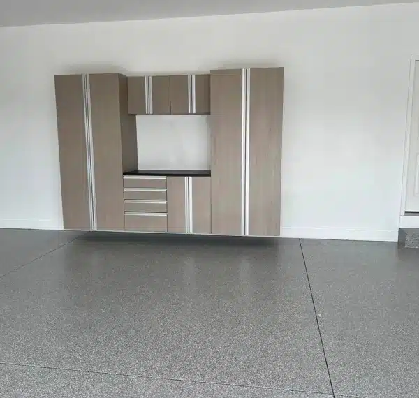 A modern, empty room with a built-in wooden wall unit containing shelves and cabinets, a speckled gray floor, white walls, and a closed door.