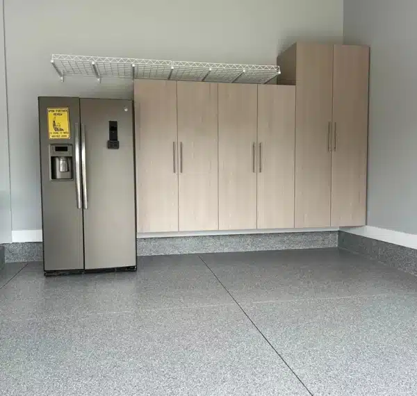 A commercial refrigerator stands beside wooden cabinets in a room with terrazzo flooring, and there's a folding chair and phone on the wall.