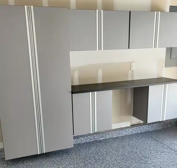 Modular garage storage system with closed and open shelves, a black countertop, and vertical handles, against a white wall on speckled flooring.