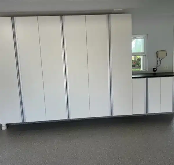 This image depicts an interior with white cupboards and a countertop, visible against a gray floor. A window offers a view of greenery outside.